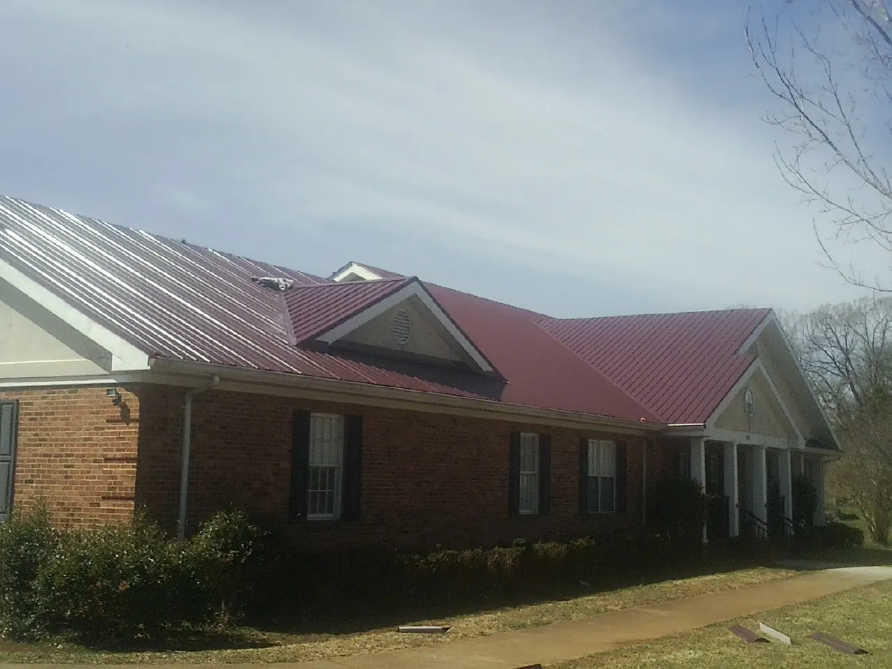 Red metal roof with gabled entries on a long brick building, from a Hail Damage Roof Repair job in Ibapah