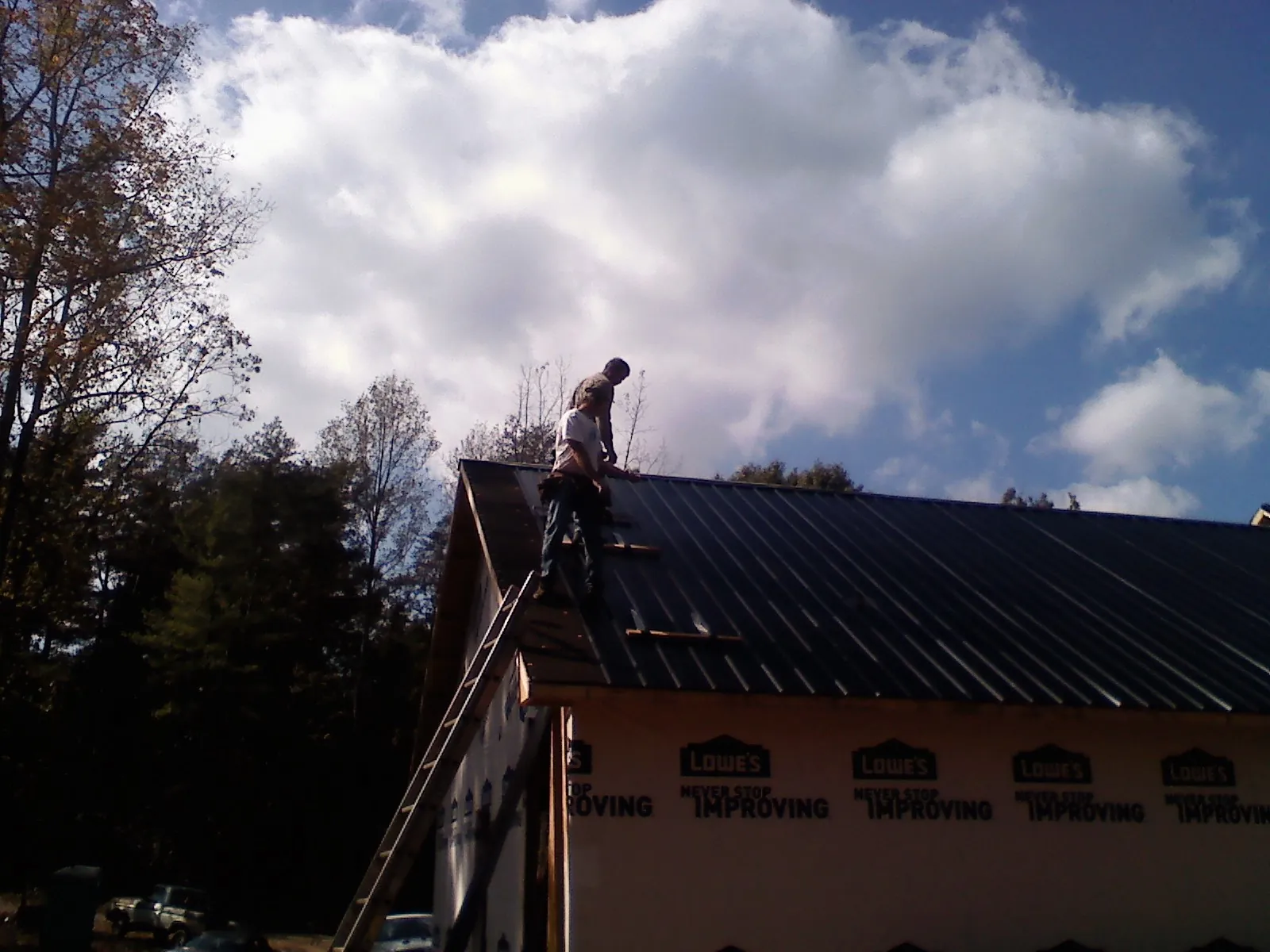 Roofer fastening dark metal panels high against a cloudy sky, from a Roof Inspection job in Ibapah