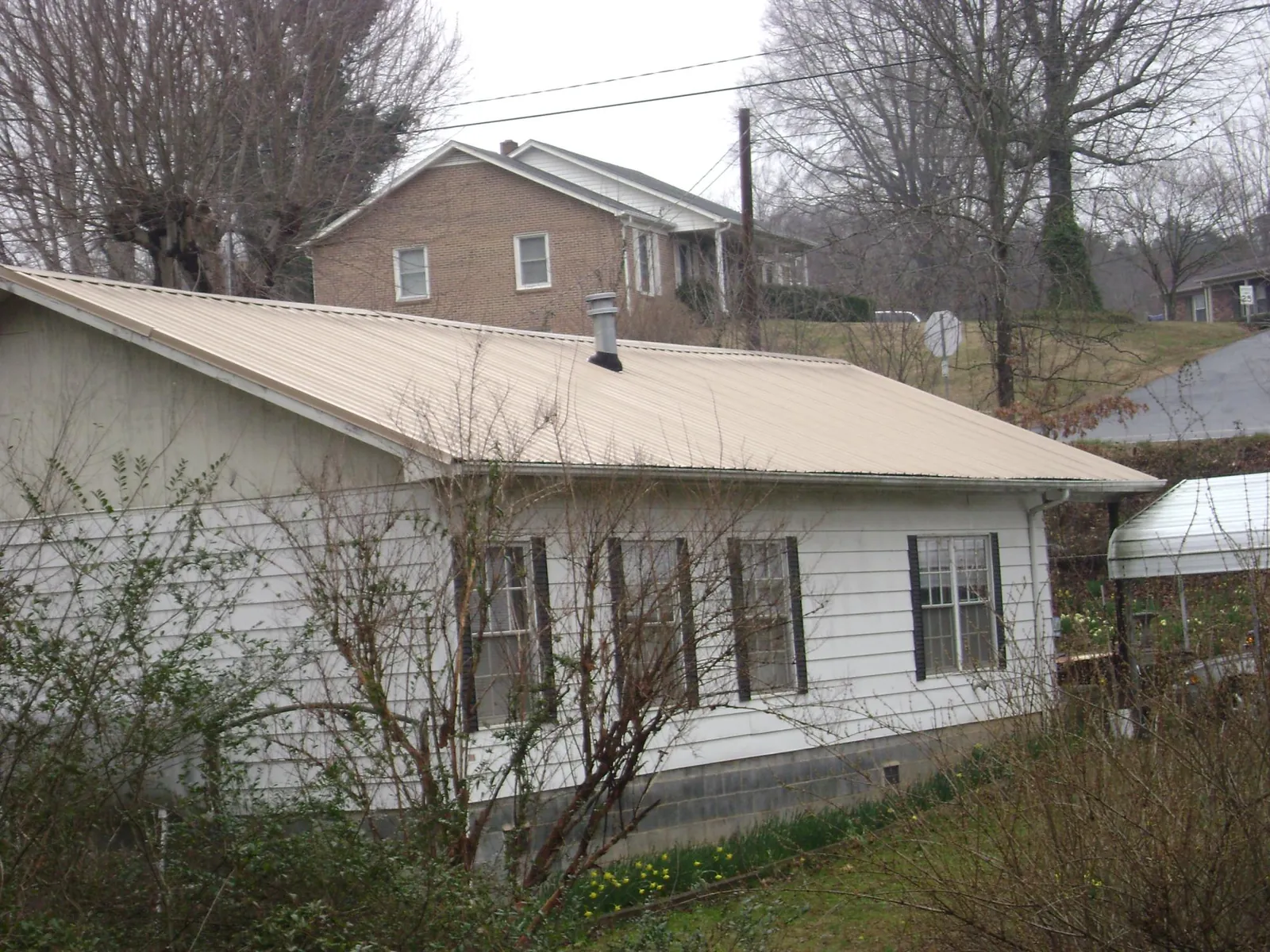 Tan metal roof on a white sided house set into a hillside — Commercial Roofing by Roofing Brothers in Ibapah